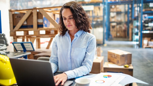 woman typing on a laptop in a warehouse