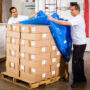 workers covering a pallet of boxes in plastic